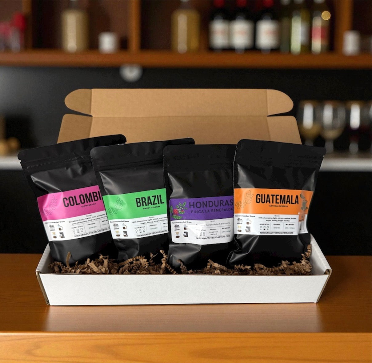 A premium coffee sample pack featuring four fresh-roasted single-origin specialty beans from the Americas: Colombia, Brazil, Honduras and Guatemala. Each bag is labeled with origin, roast date, and tasting notes. The sample pack is displayed in a kraft gift tray with shredded paper filler, highlighting the brand’s commitment to quality and freshness. Ideal for gifting or exploring regional flavor profiles at home